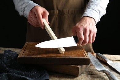 Photo of Man sharpening knife with sharpener on wooden table, closeup