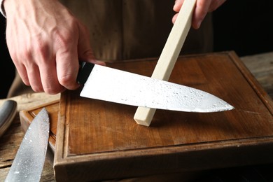 Photo of Man sharpening knife with sharpener on wooden table, closeup