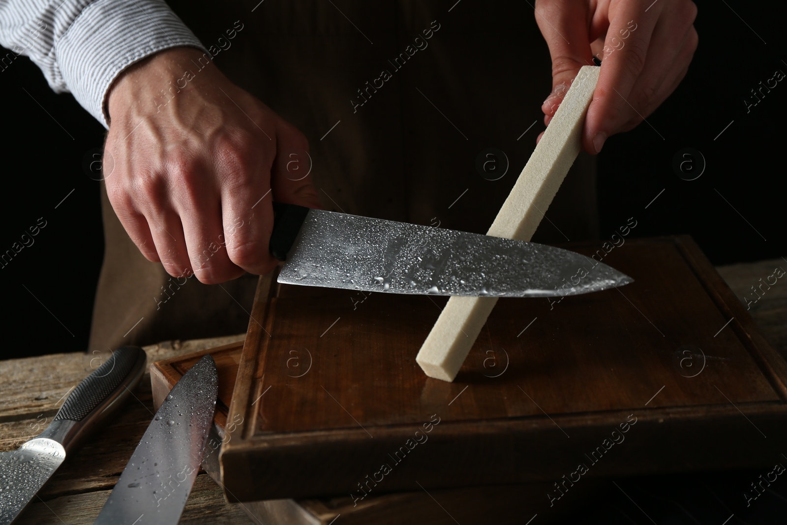 Man sharpening knife with sharpener on wooden table, closeup Photo of Man sharpening knife with sharpener on wooden table, closeup