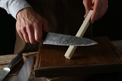 Photo of Man sharpening knife with sharpener on wooden table, closeup