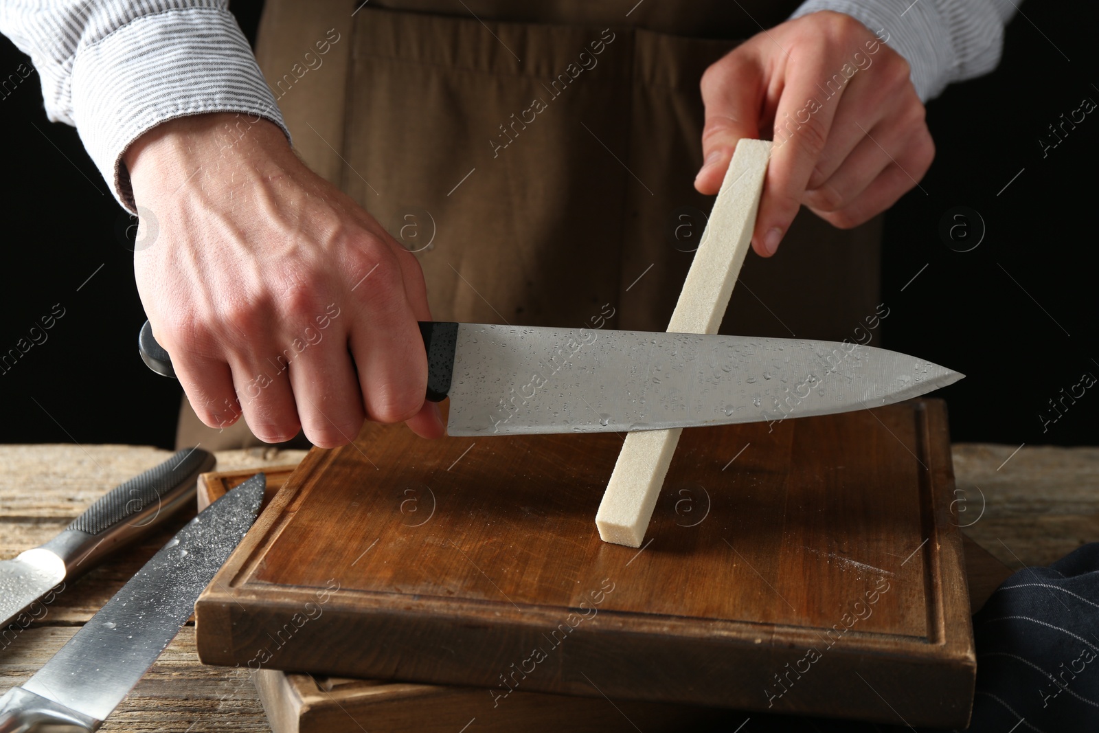 Man sharpening knife with sharpener on wooden table, closeup Photo of Man sharpening knife with sharpener on wooden table, closeup