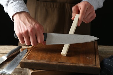 Photo of Man sharpening knife with sharpener on wooden table, closeup