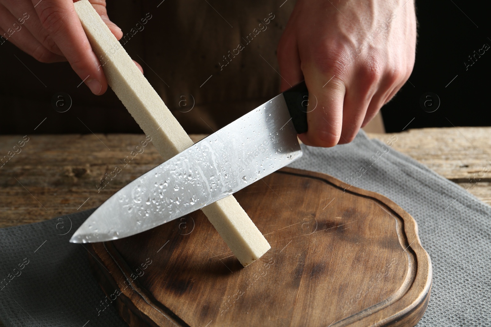 Man sharpening knife with sharpener on wooden table, closeup Photo of Man sharpening knife with sharpener on wooden table, closeup
