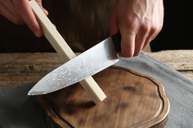 Photo of Man sharpening knife with sharpener on wooden table, closeup