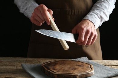 Photo of Man sharpening knife with sharpener on wooden table, closeup
