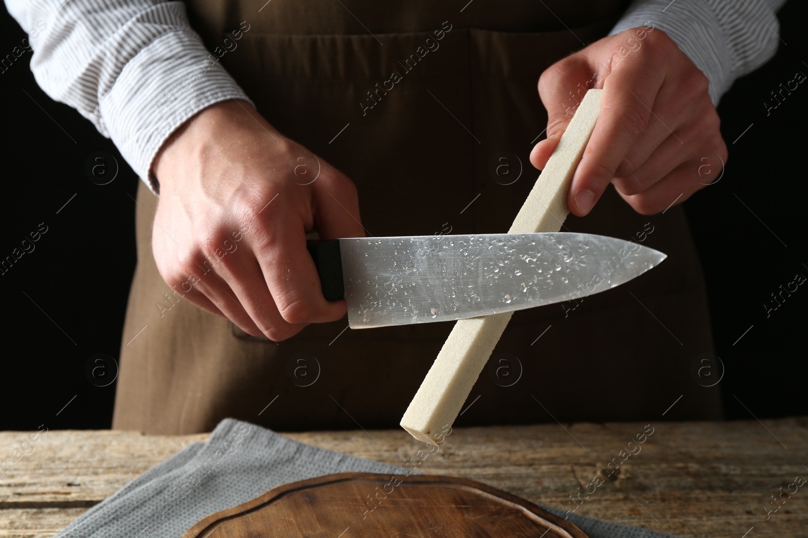 Man sharpening knife with sharpener on wooden table, closeup Photo of Man sharpening knife with sharpener on wooden table, closeup