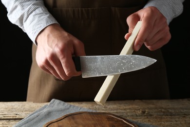 Photo of Man sharpening knife with sharpener on wooden table, closeup