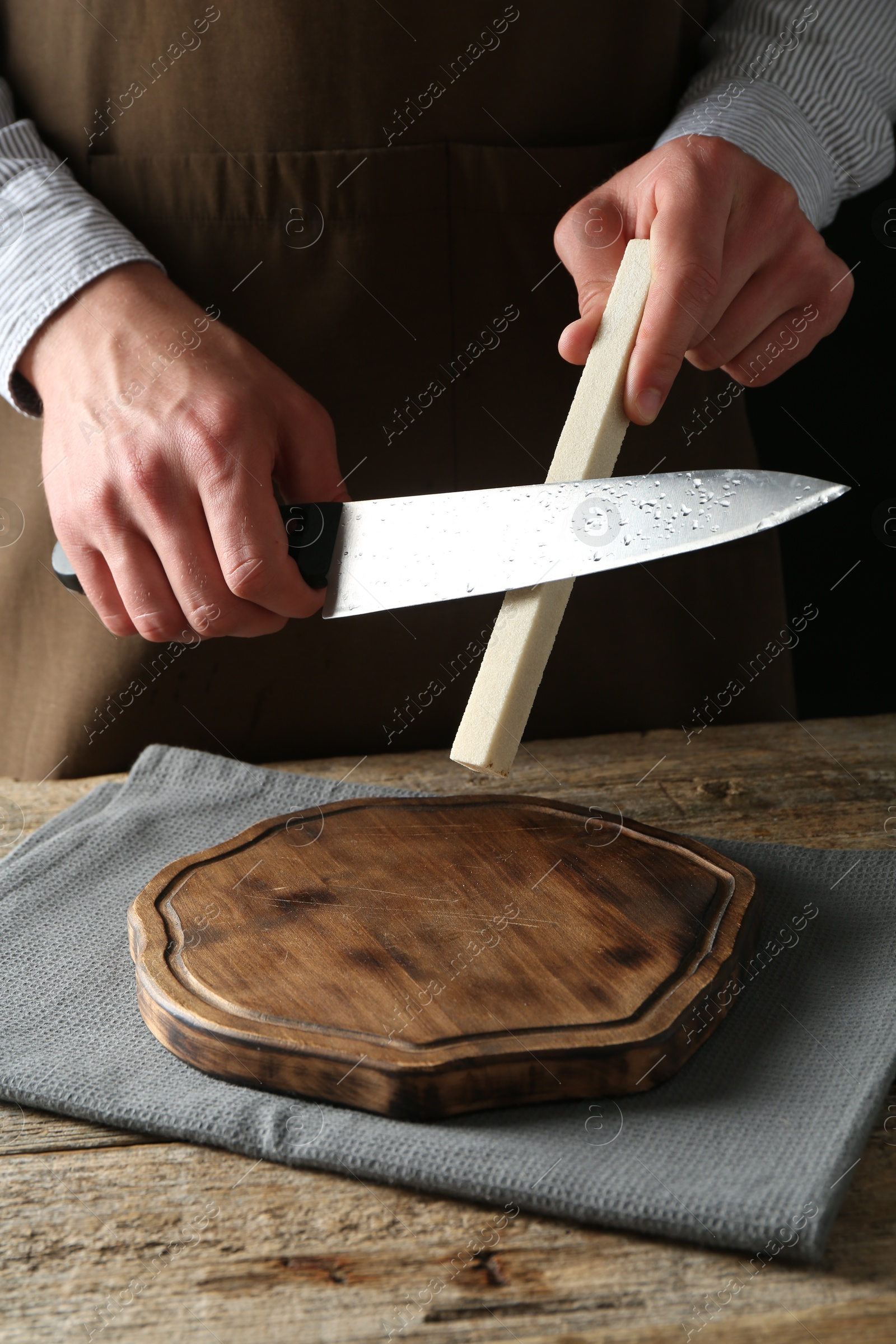 Man sharpening knife with sharpener on wooden table, closeup Photo of Man sharpening knife with sharpener on wooden table, closeup