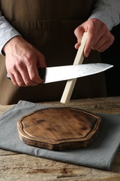 Photo of Man sharpening knife with sharpener on wooden table, closeup
