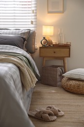 Photo of Comfortable bed with soft linens, slippers and bedside table in room. Home textile