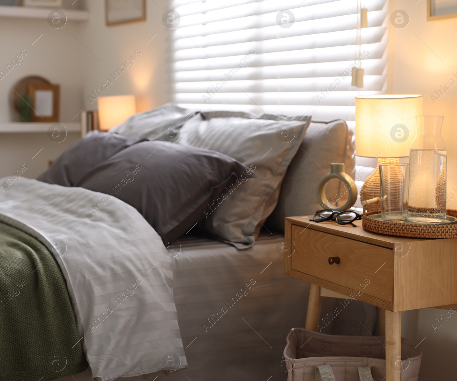 Comfortable bed with soft linens, bedside table and lamp in room. Home textile Photo of Comfortable bed with soft linens, bedside table and lamp in room. Home textile
