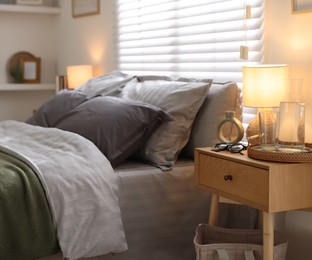 Photo of Comfortable bed with soft linens, bedside table and lamp in room. Home textile