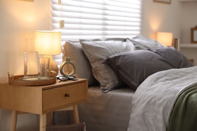 Photo of Comfortable bed with soft linens, bedside table and lamp in room. Home textile