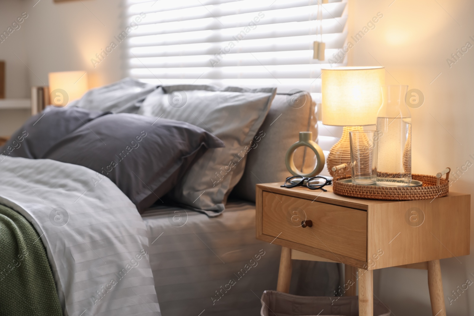 Comfortable bed with soft linens, bedside table and lamp in room. Home textile Photo of Comfortable bed with soft linens, bedside table and lamp in room. Home textile