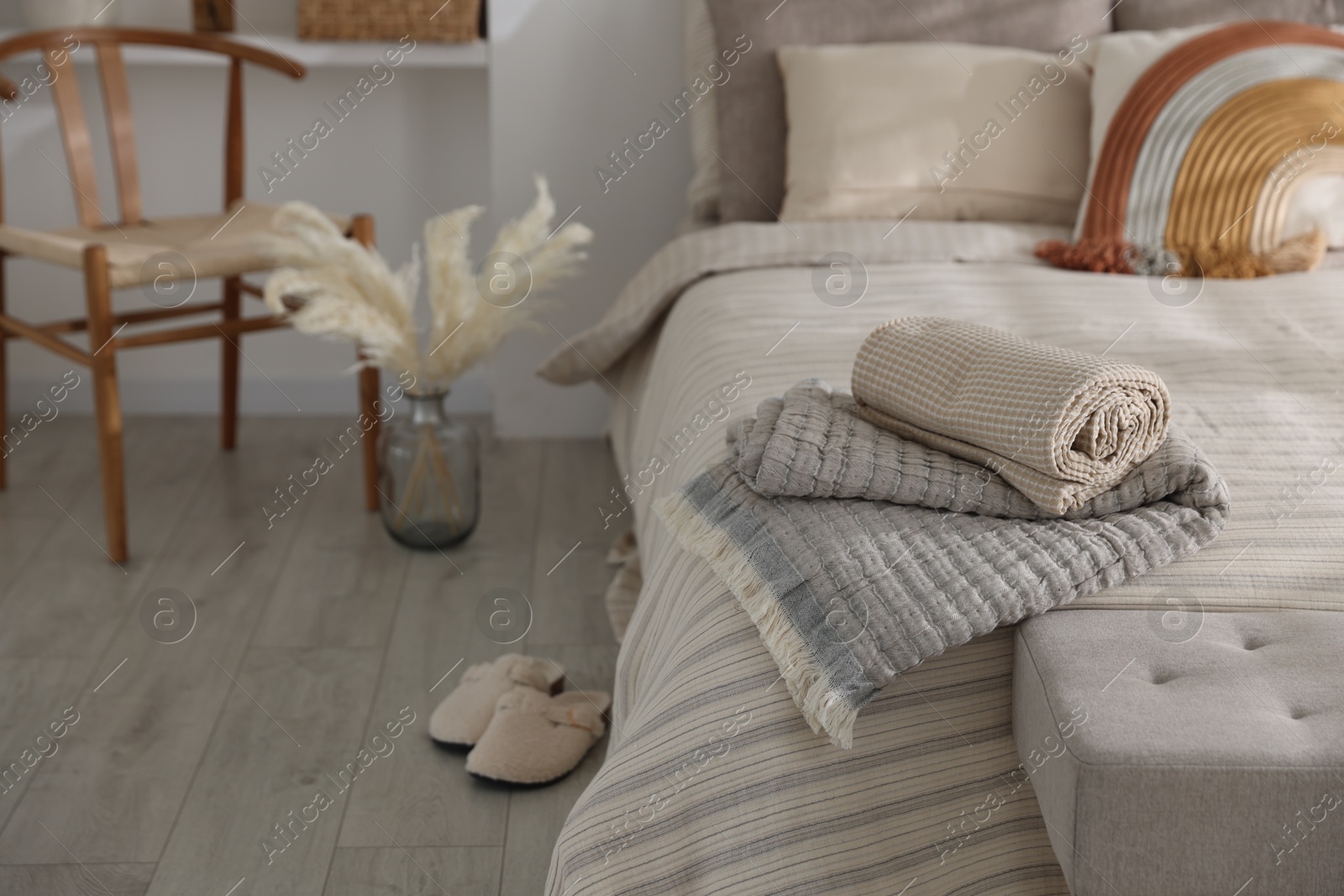 Comfortable bed with soft linens, slippers and decor in room. Home textile Photo of Comfortable bed with soft linens, slippers and decor in room. Home textile