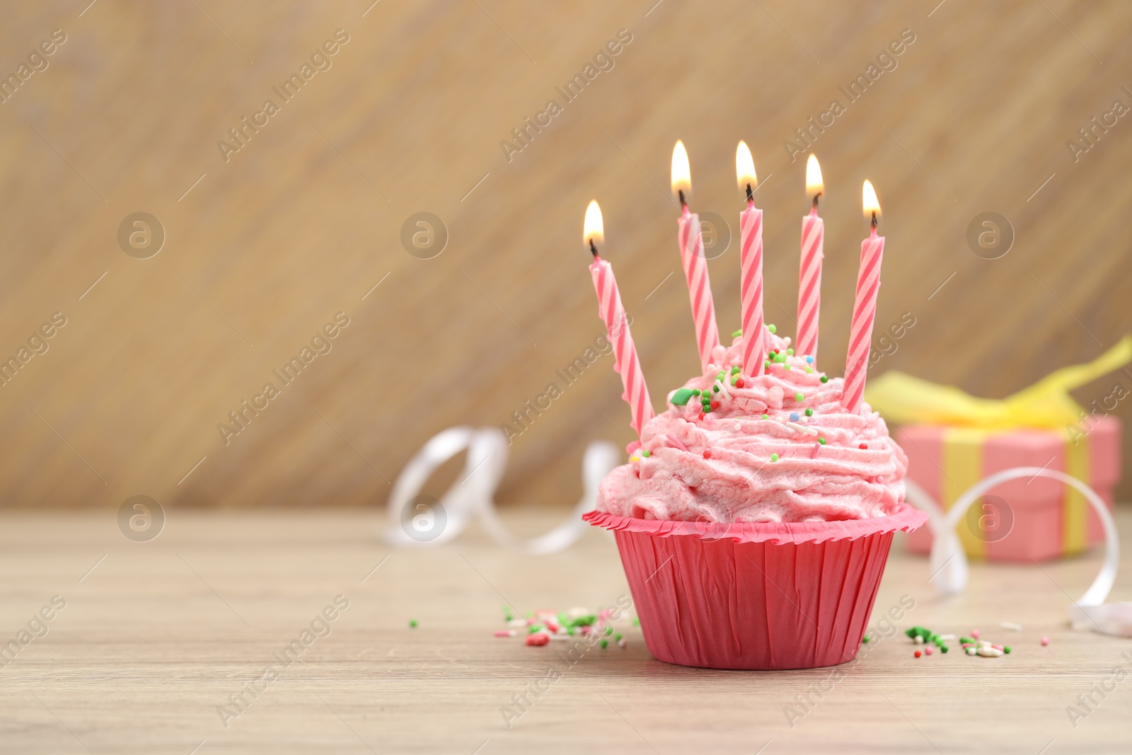 Photo of Burning candles in cupcake, sprinkles and party decor on wooden table, space for text