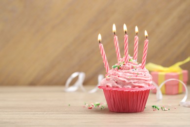 Photo of Burning candles in cupcake, sprinkles and party decor on wooden table, space for text