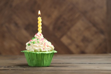 Photo of Burning candle in cupcake on wooden table, space for text