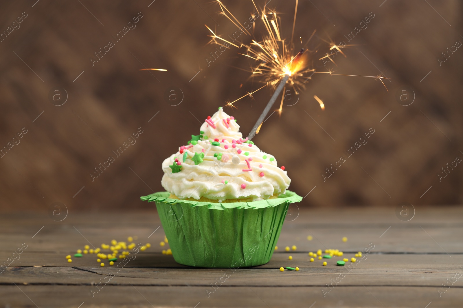 Burning sparkler in cupcake and sprinkles on wooden table Photo of Burning sparkler in cupcake and sprinkles on wooden table