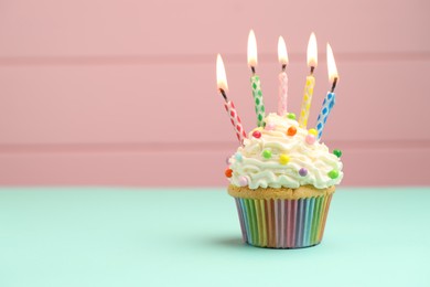 Photo of Burning candles in cupcake on turquoise table against pink background, space for text