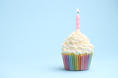 Photo of Burning candle in cupcake on light blue background, space for text