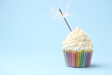 Photo of Burning sparkler in cupcake on light blue background, space for text