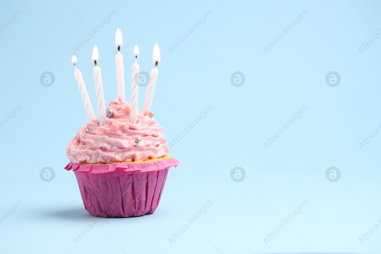 Photo of Burning candles in cupcake on light blue background, space for text