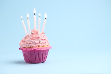 Photo of Burning candles in cupcake on light blue background, space for text