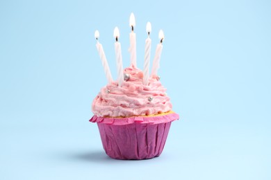 Photo of Burning candles in cupcake on light blue background