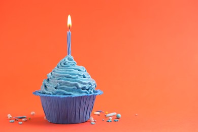 Photo of Burning candle in cupcake and sprinkles on orange background, space for text
