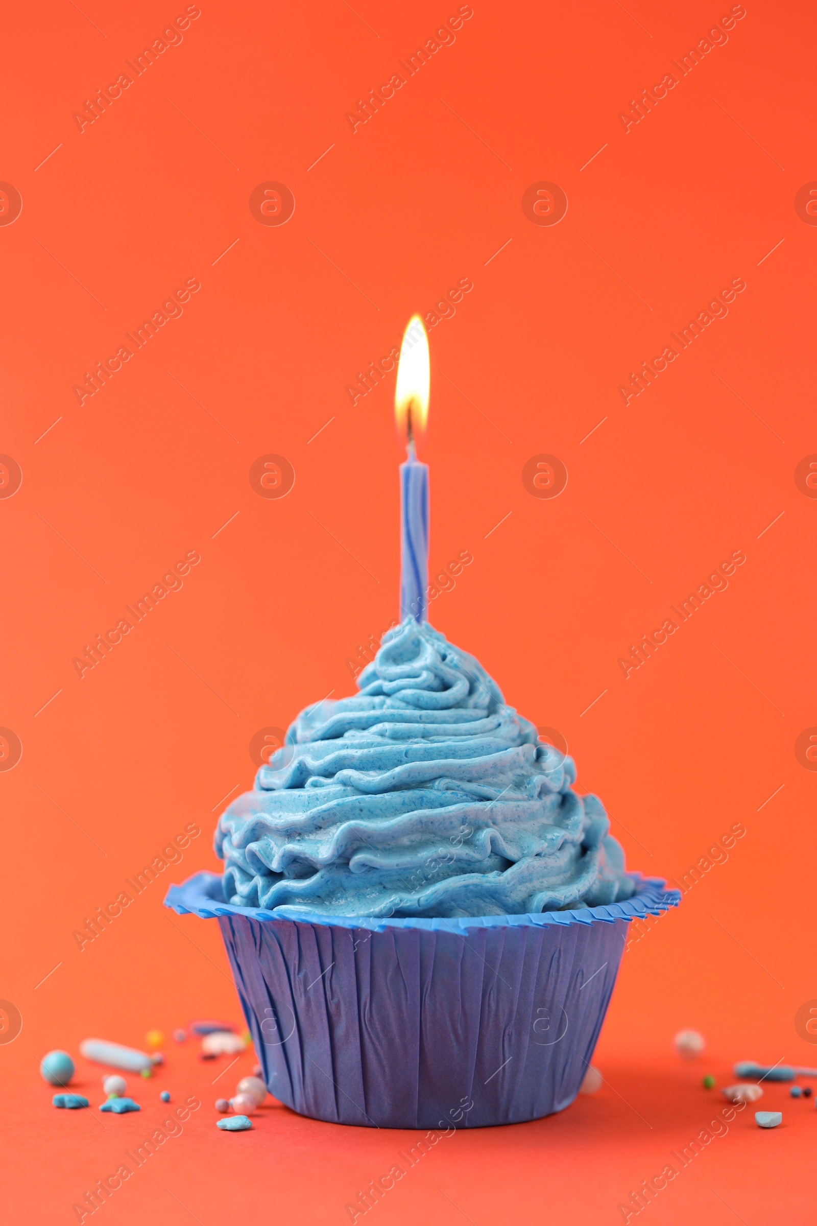 Photo of Burning candle in cupcake and sprinkles on orange background