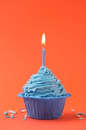 Photo of Burning candle in cupcake and sprinkles on orange background