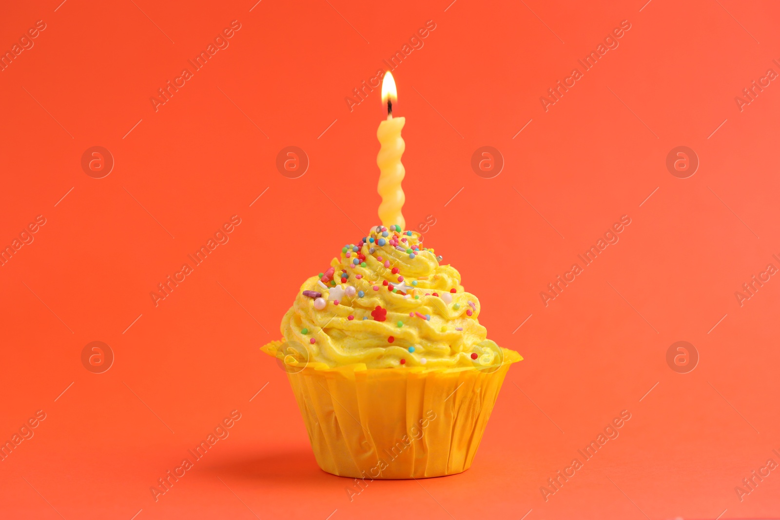 Photo of Burning candle in cupcake on orange background