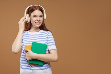 Photo of Teenage girl with headphones and books on brown background. Space for text