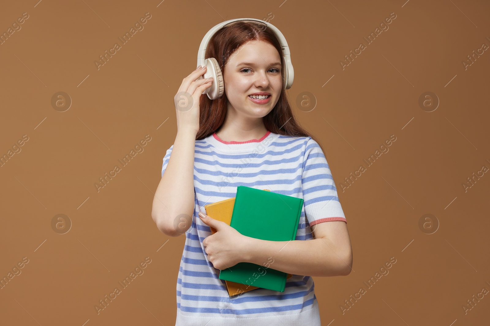 Teenage girl with headphones and books on brown background Photo of Teenage girl with headphones and books on brown background