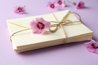 Photo of Stack of love letters and carnation flowers on violet background, closeup