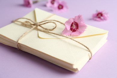 Photo of Stack of love letters and carnation flowers on violet background, closeup