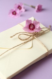 Photo of Stack of love letters and carnation flowers on violet background, closeup