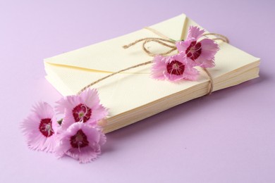 Photo of Stack of love letters and carnation flowers on violet background, closeup