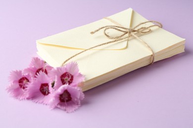 Photo of Stack of love letters and carnation flowers on violet background, closeup