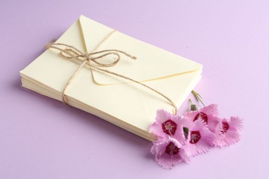 Photo of Stack of love letters and carnation flowers on violet background, closeup