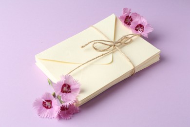 Photo of Stack of love letters and carnation flowers on violet background, closeup
