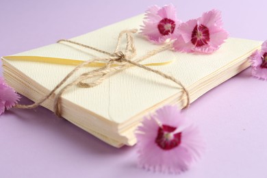Photo of Stack of love letters and carnation flowers on violet background, closeup