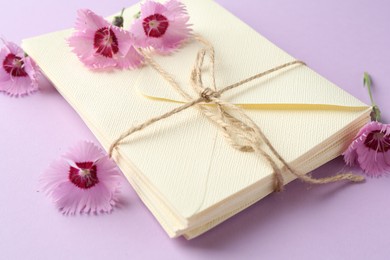 Photo of Stack of love letters and carnation flowers on violet background, closeup