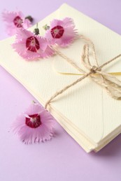 Photo of Stack of love letters and carnation flowers on violet background, closeup