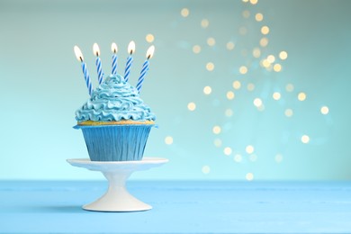Photo of Burning candles in cupcake on light blue table against turquoise background with blurred lights, space for text