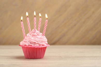 Photo of Burning candles in cupcake on wooden table, space for text