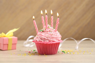 Photo of Burning candles in cupcake, sprinkles and party decor on wooden table