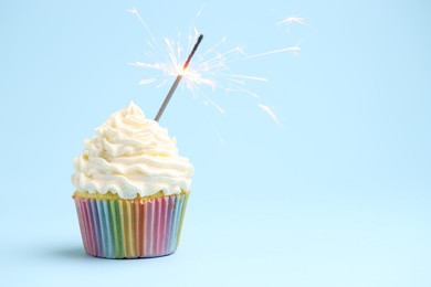 Photo of Burning sparkler in cupcake on light blue background, space for text