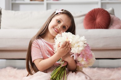 Photo of Cute little girl with bouquet of beautiful peonies on floor at home